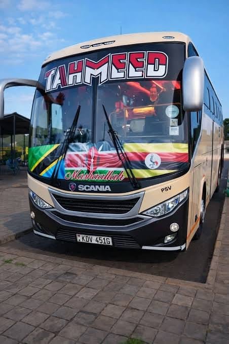 Cream and black Scania bus with Mahmeed branding and colorful African stripe design parked on a brick surface