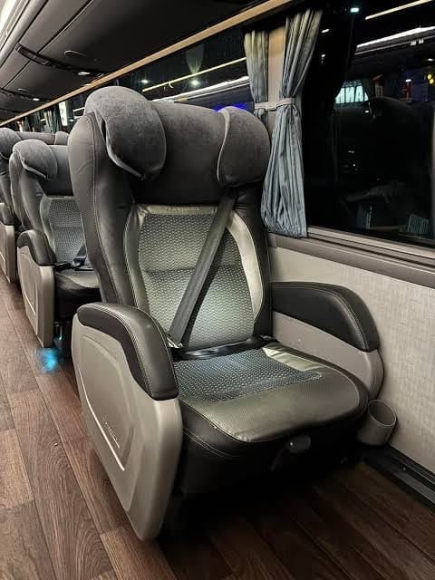 Comfortable coach bus seat with gray and black upholstery, headrest pillow, and window beside it